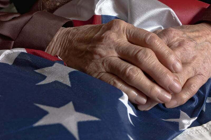 An elderly veteran's hands rest on an American flag