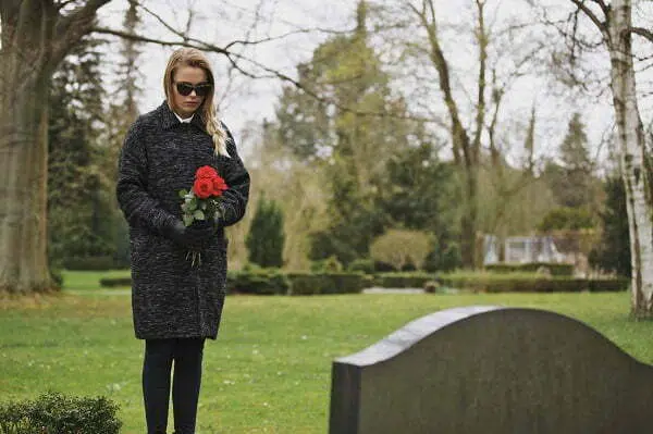 Widow holding roses standing in front of gravestone