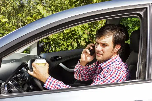 Man talking on the phone with his coffee on his other hand and driving at the same time