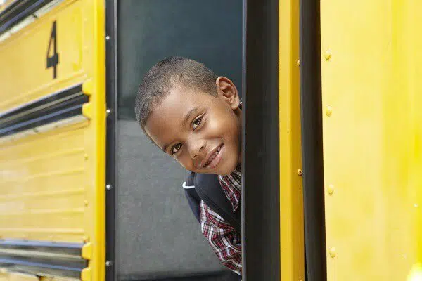 Young elementary school student on the school bus looking out the door and smiling