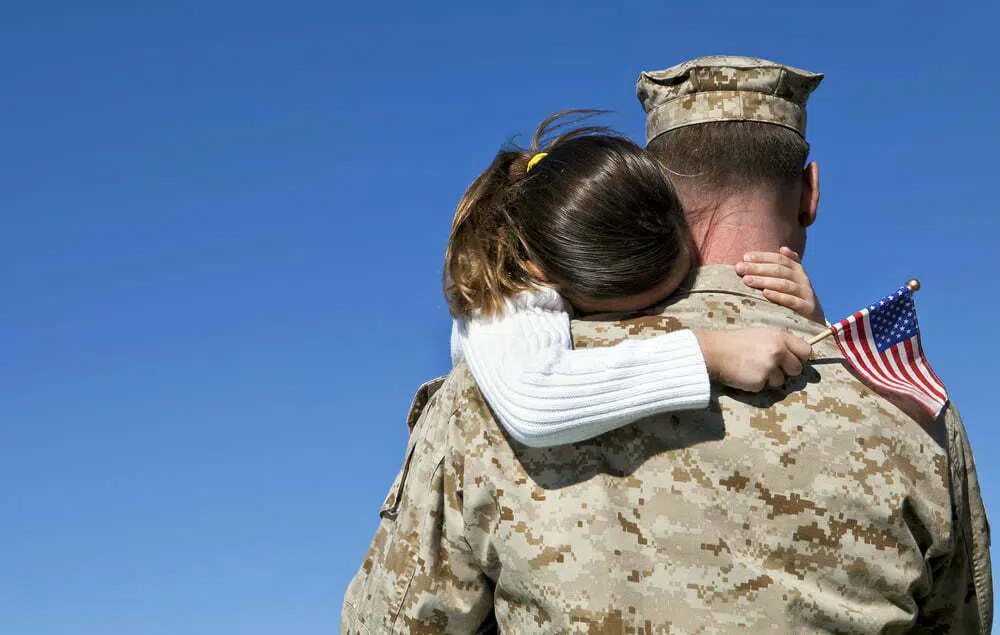 View from behind of daughter hugging her military father, sad because he has lost his hearing
