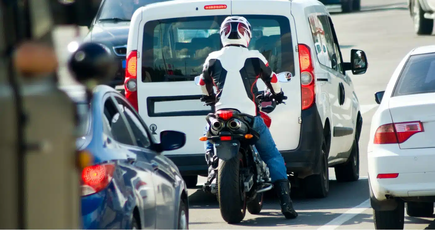 A motorcycle driver waiting in traffic between automobiles