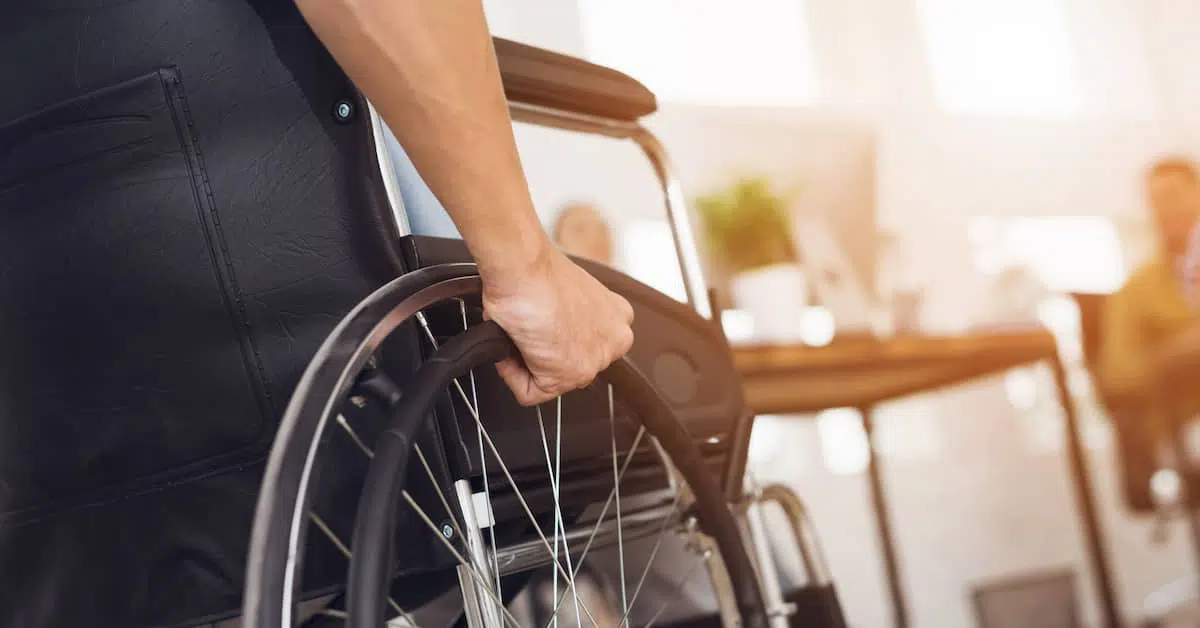 A close up look of a wheelchair with right hand on the wheel