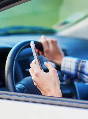 A male texting while holding onto the steering wheel