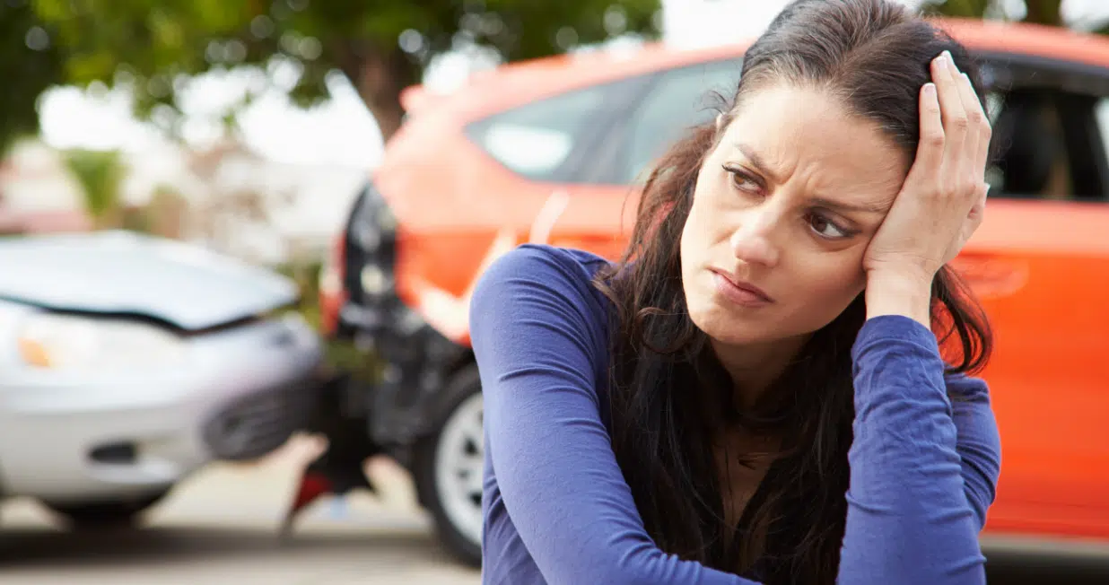 A distraught woman thinking about what to do with the car accident in the background