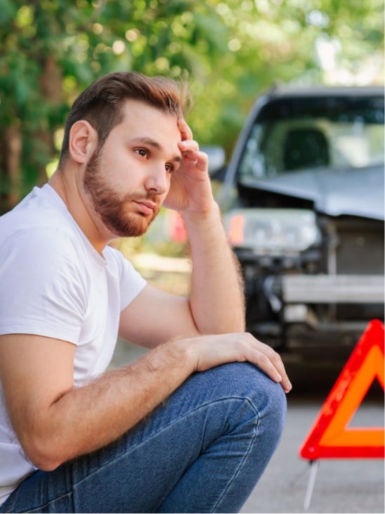 a man sitting by a car after a car accident
