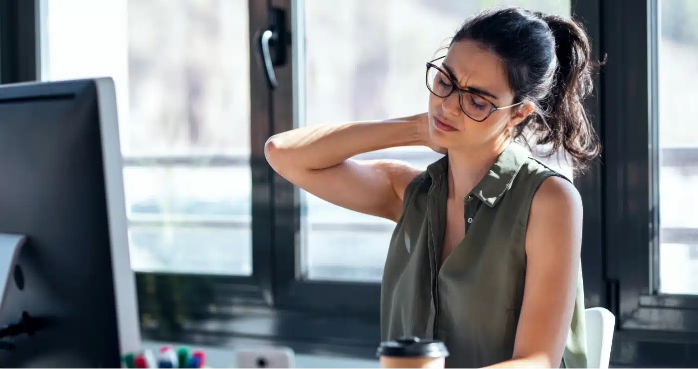 A woman sitting at a desk and experiencing neck pain