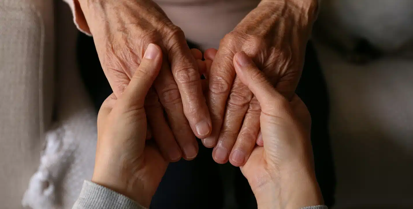 Closeup of the hands of a younger person holding the hands of an elderly person
