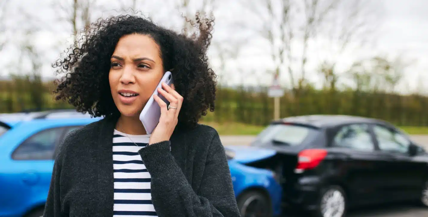 A woman on the phone near two cars that have been in a crash