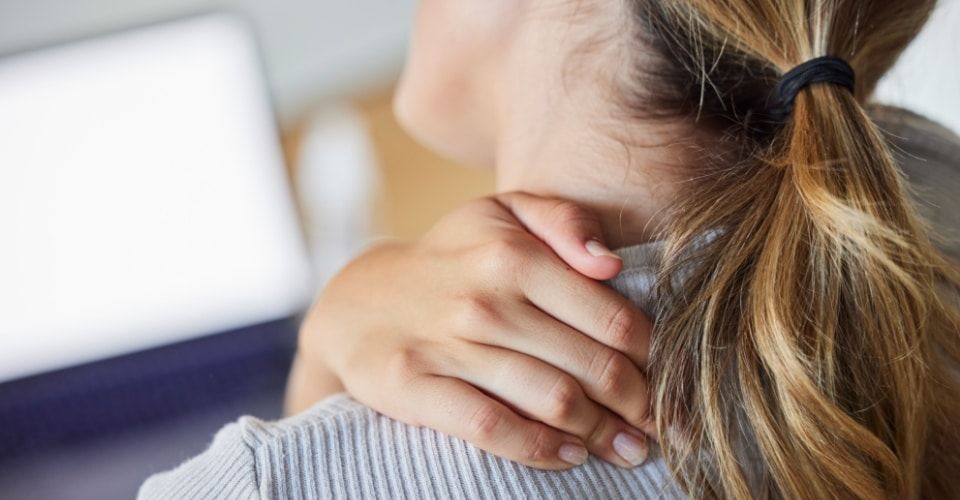 Close-up of a person with her hand on her neck experiencing neck pain