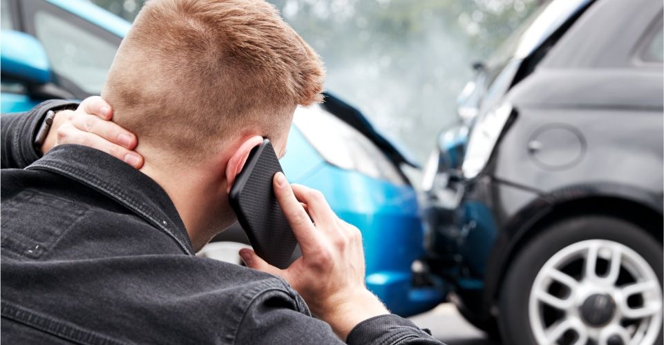 Man holding phone near car accident scene, illustrating distracted driving and potential injuries.