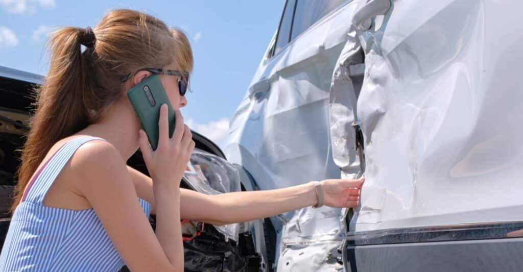 a woman on the phone looking at damage from a car accident